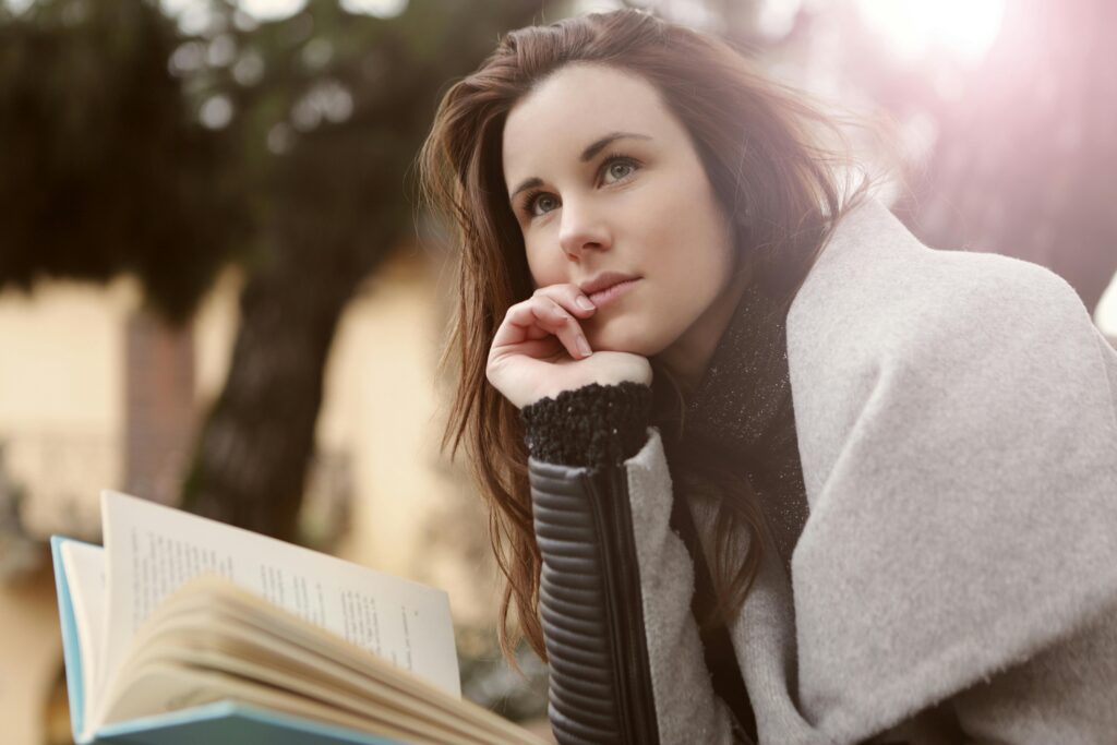 A young woman in deep thought while reading outdoors, captured in warm daylight.