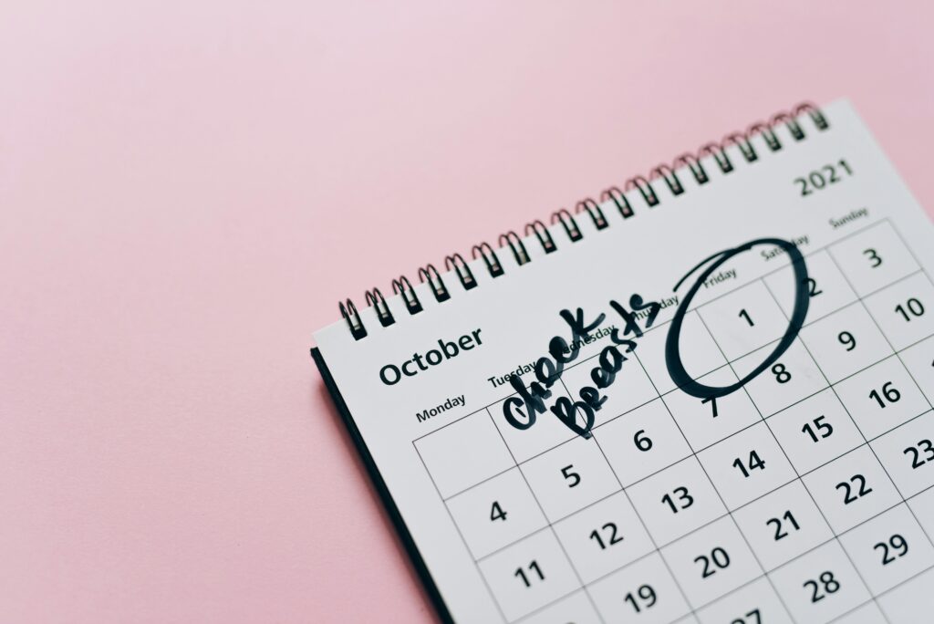 October calendar with breast check reminder, emphasizing health awareness on a pink background.