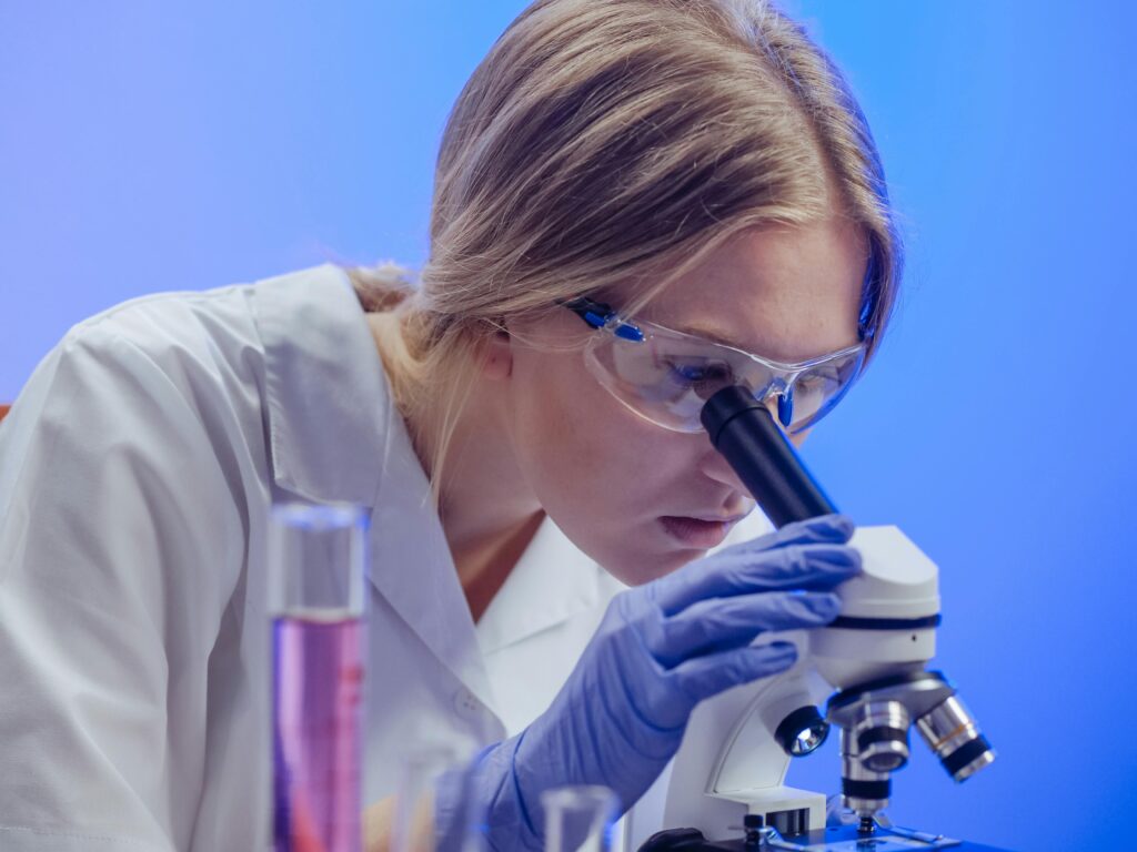 A female scientist in protective gear using a microscope in a laboratory setting.