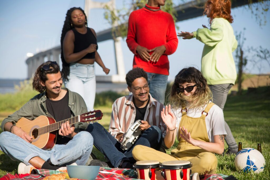 Diverse group of friends playing musical instruments and enjoying a picnic by the river in Portugal.