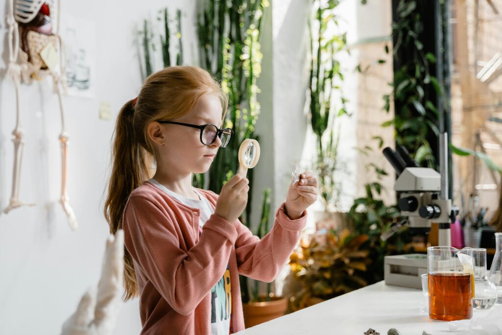 A young girl uses a magnifying glass to study samples in a vibrant indoor lab environment.