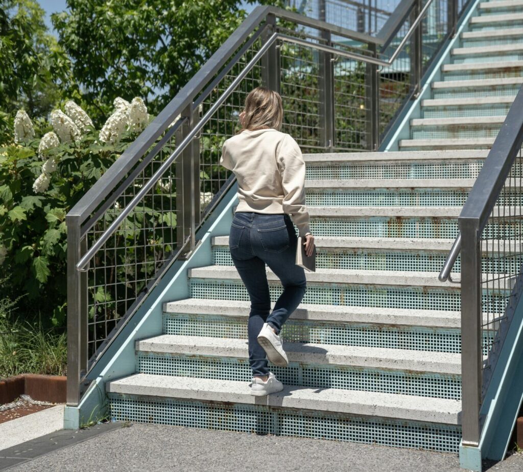 Rear view of a person ascending stairs in a greenery-filled urban park setting.